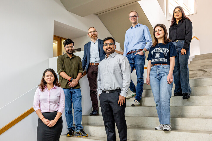 Sieben Personen stehen auf einer Treppe in einem Universitätsgebäude. Hinten links steht Thilo Dieing. Er trägt ein hellblaues Hemd.